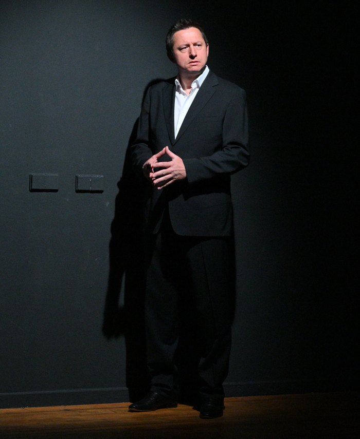 Alexander Nikolaus on stage, in a suit against the dark wall.